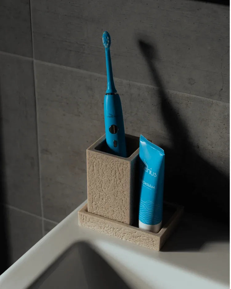 Invenius S50 i en tandborstmugg av sten bredvid Invenius tandkräm vid handfatet